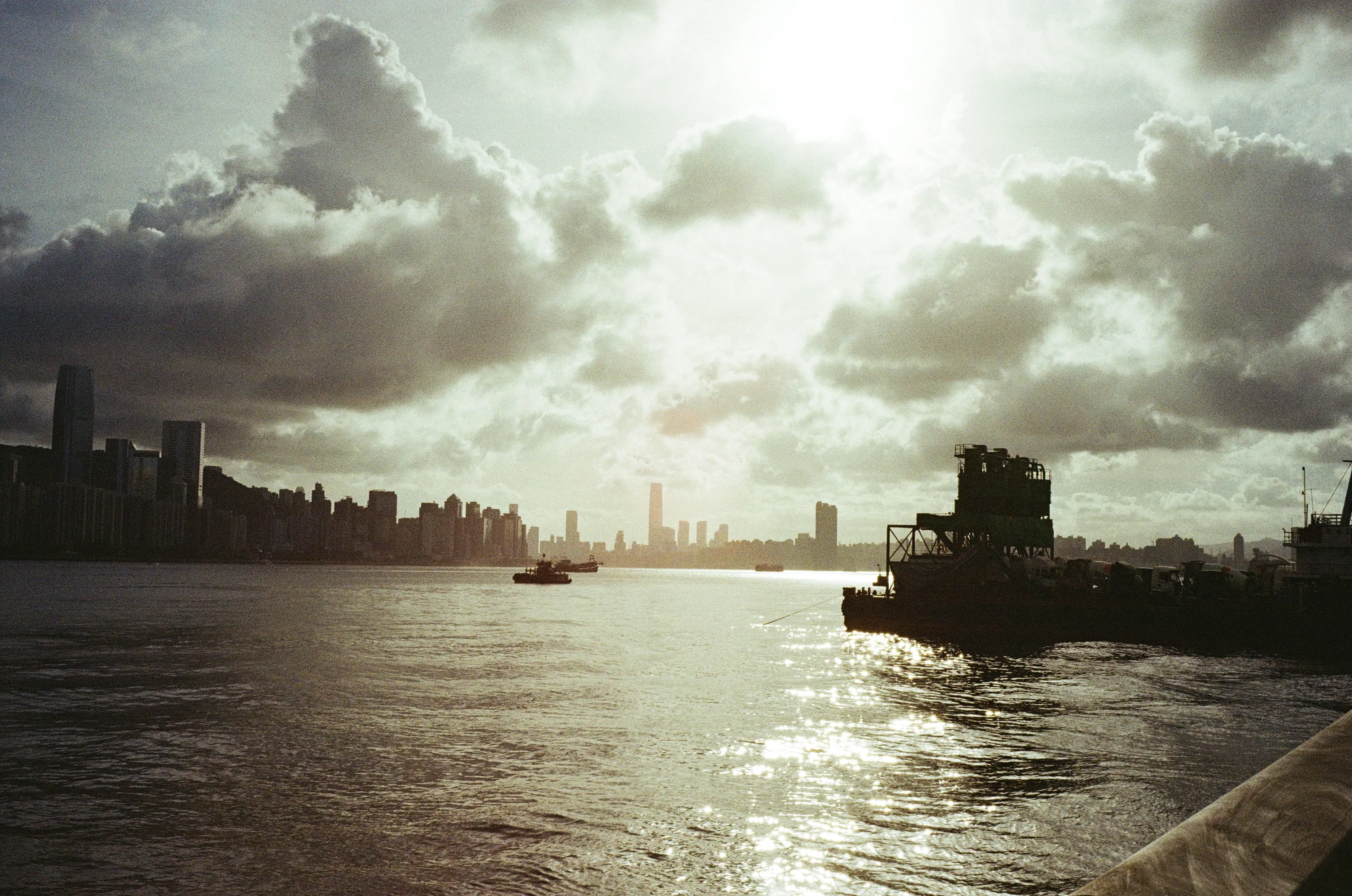 Harbor skyline under dramatic clouds, boats crossing the water