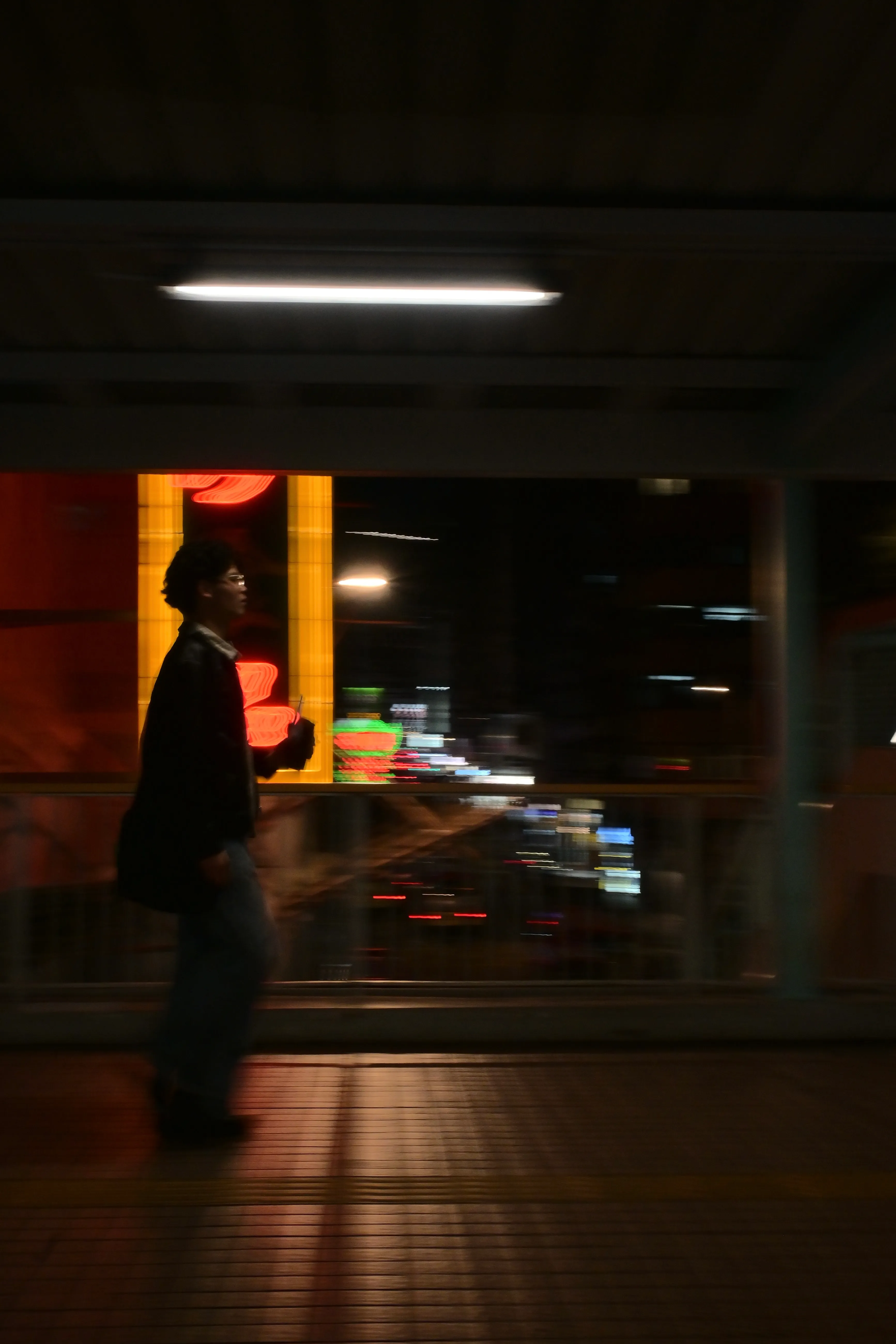 Person walking across a footbridge at night, neon signs behind
